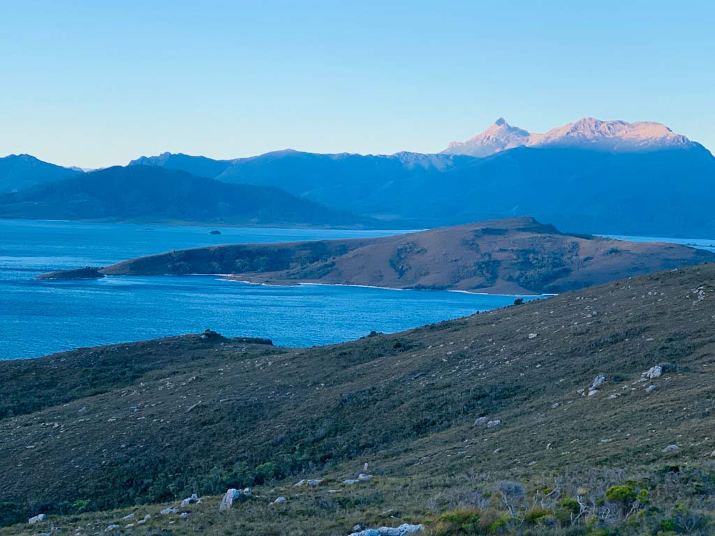 A lake below green hills and distant mountains.