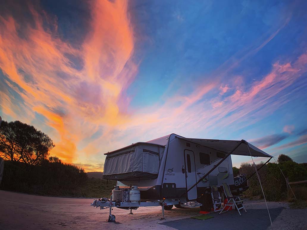A camper trailer set up under a bright sunset sky.